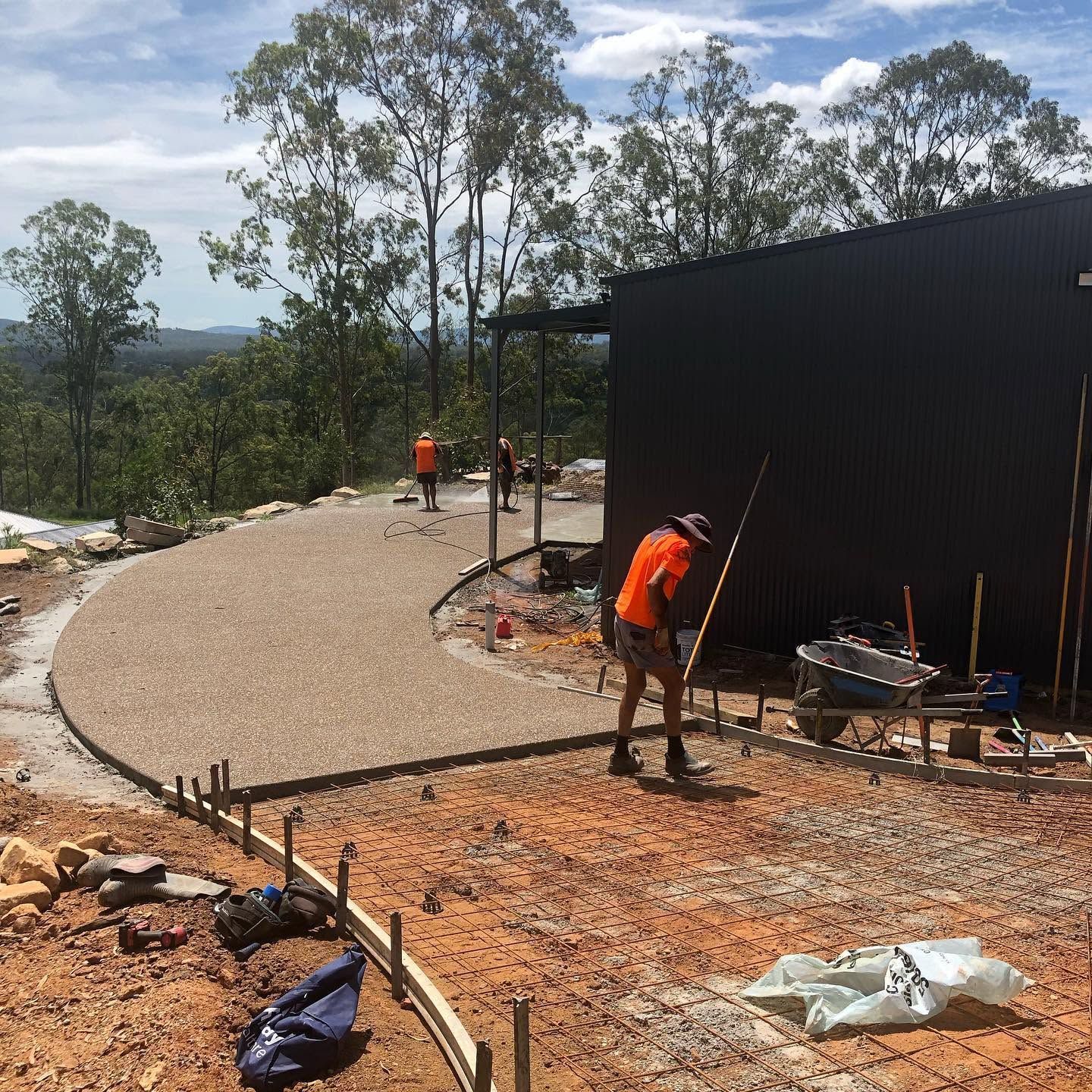 Workers in orange vests landscaping beside a black building and curved gravel path