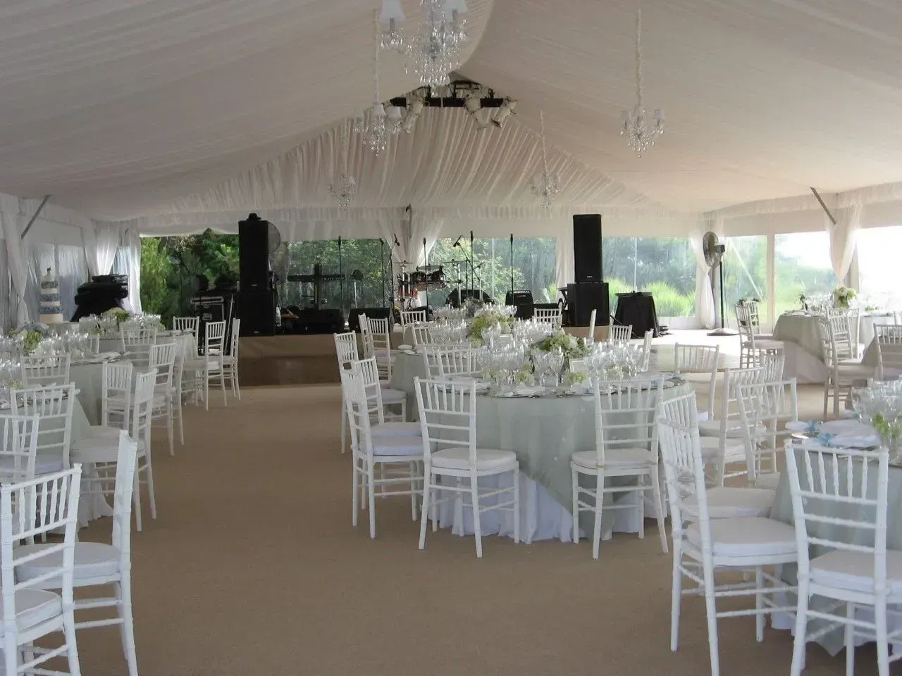 An elegant wedding reception tent with white chairs, draped ceilings, crystal chandeliers, and round tables.