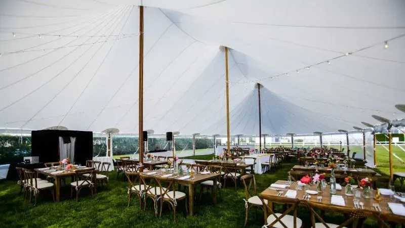 Outdoor event tent set up with rows of wooden tables and chairs on grass, decorated for a gathering.