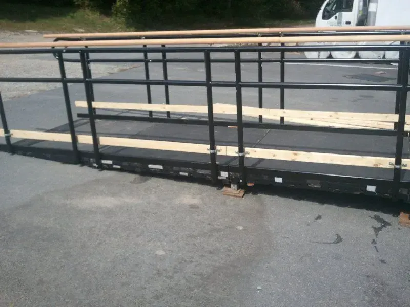 A black metal wheelchair ramp with temporary wooden handrails set up on asphalt.