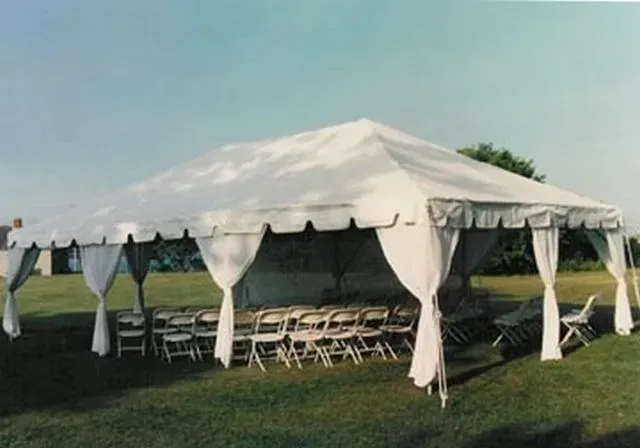 A large white event tent set up on a grassy lawn with rows of white chairs underneath.