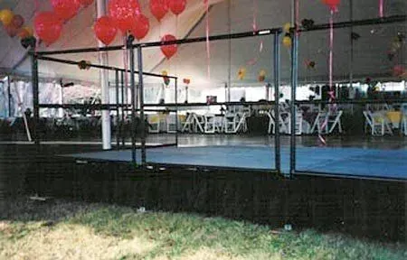 A portable wrestling ring on a stage under a tent, decorated with red and yellow balloons.