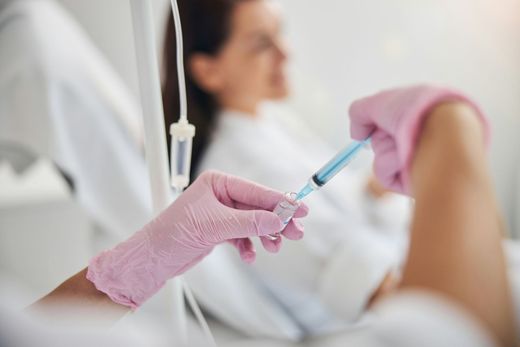 Gloved hands exchanging a syringe in a clinical setting with a blurred patient in the background