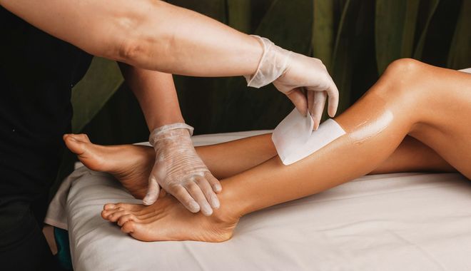 Gloved hands waxing a person’s lower leg on a treatment bed