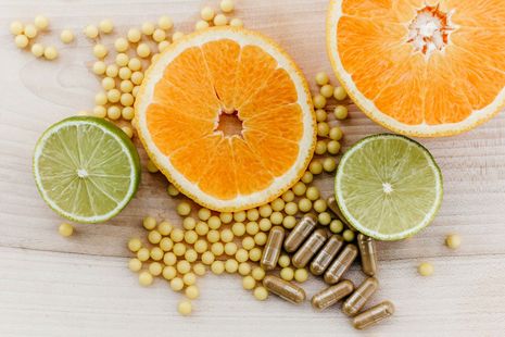 Sliced oranges and limes with scattered capsules on a light wooden surface
