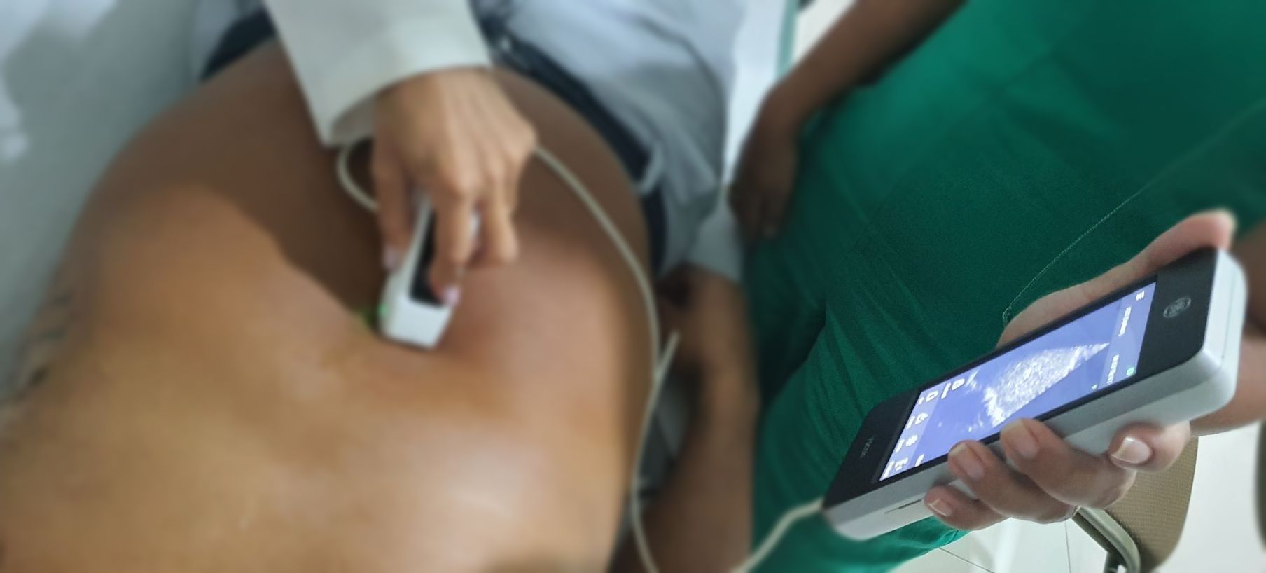 Uma pessoa recebe um ultrassom nas costas enquanto outra pessoa segura um smartphone exibindo a imagem do exame.