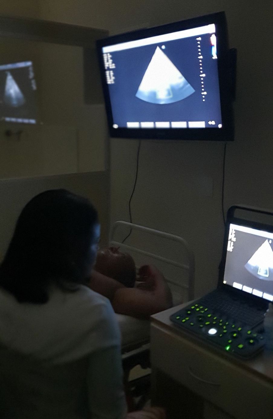 Profissional realizando um ultrassom em um paciente em um ambiente médico, com monitores exibindo os resultados do exame.