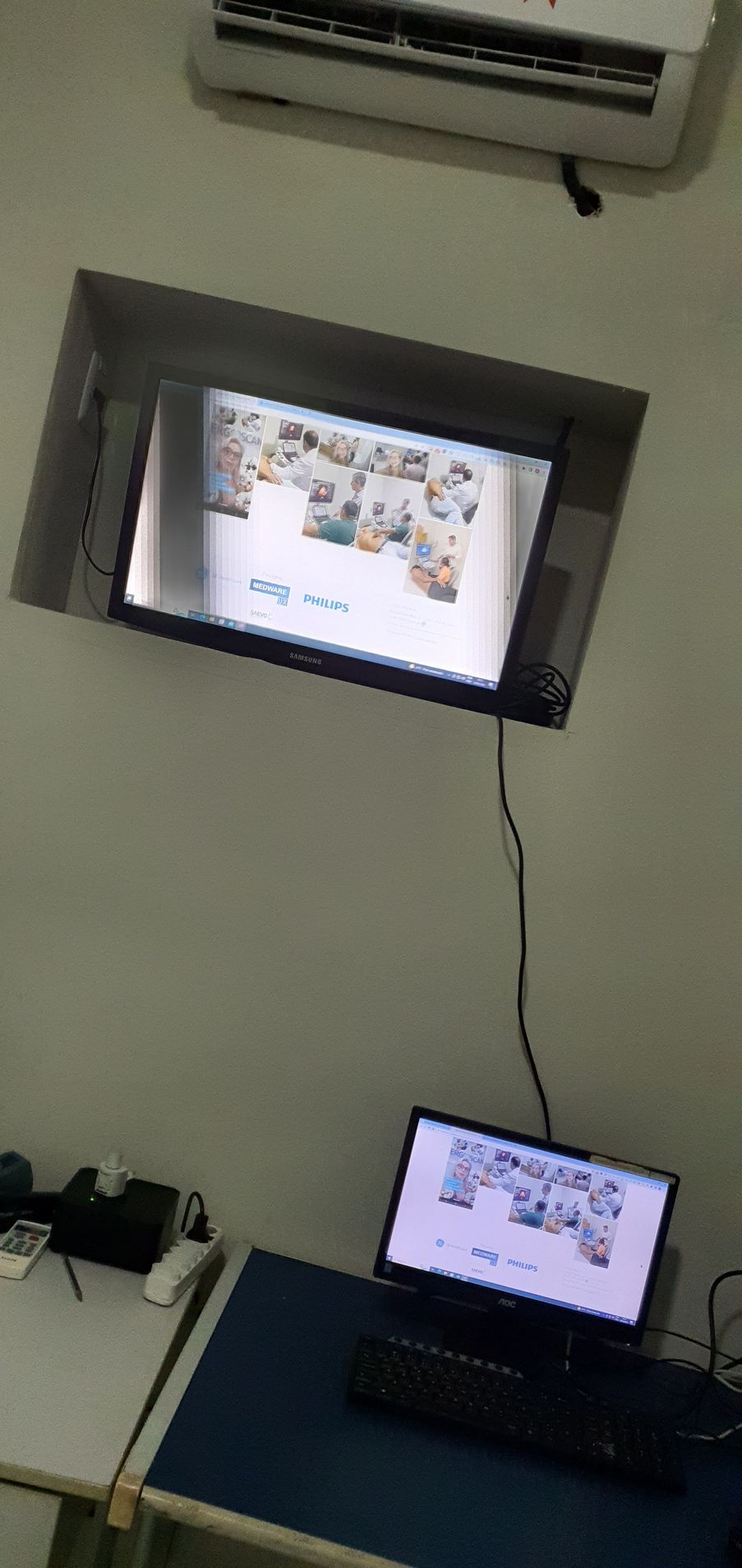 Um laptop e uma TV exibindo o mesmo conteúdo estão sobre uma mesa, com um ar-condicionado na parede acima.