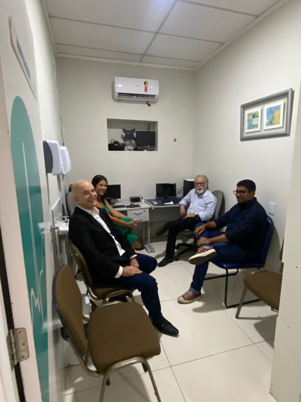 Quatro pessoas sentadas em uma pequena sala com computadores.