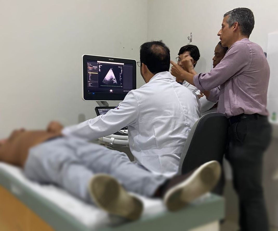 Os médicos realizam um ultrassom em um paciente em uma sala de exames. Um deles examina a tela enquanto os outros observam.