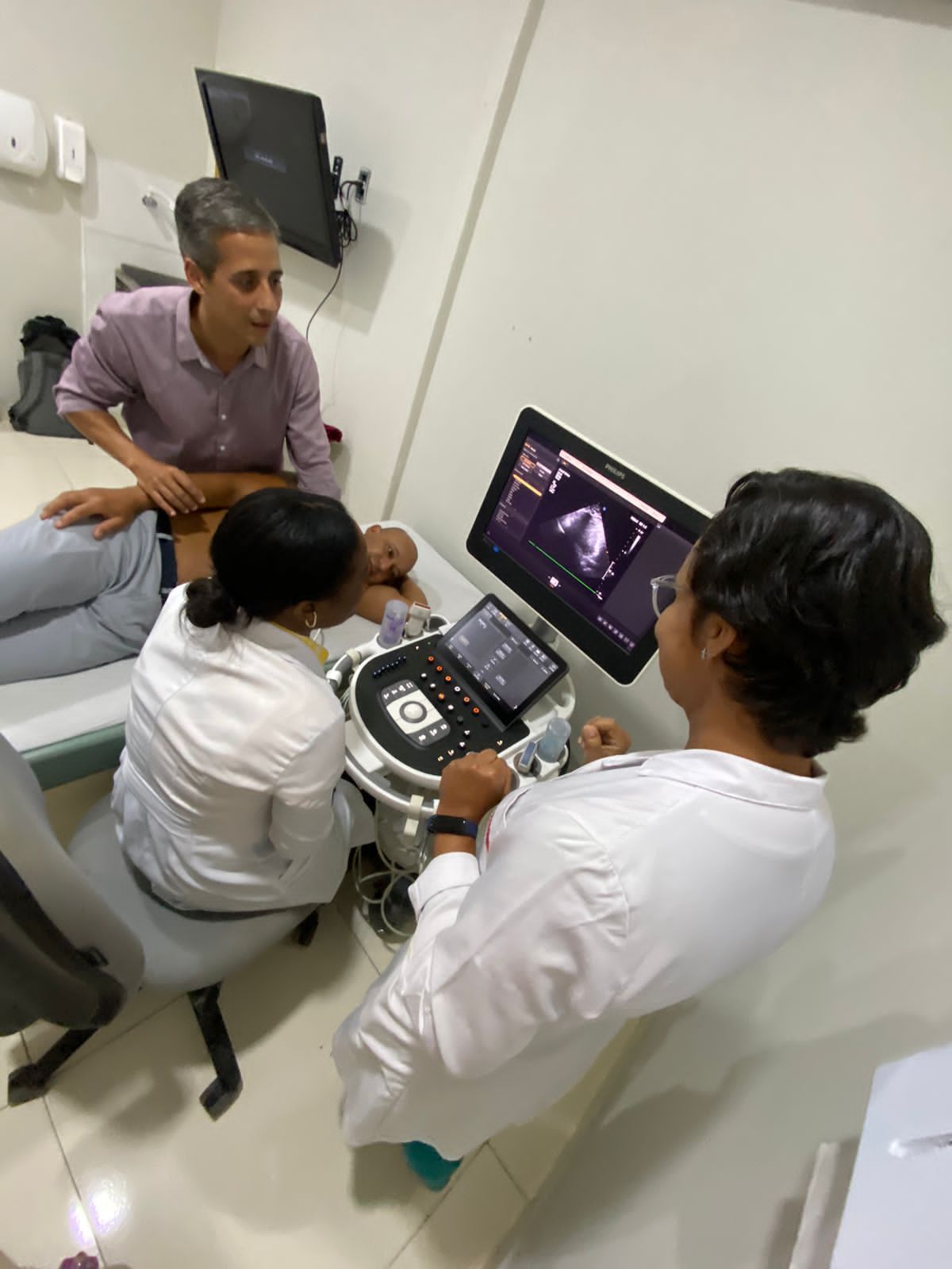 Três profissionais de saúde realizam um exame de ultrassom em um paciente em uma sala de exames.