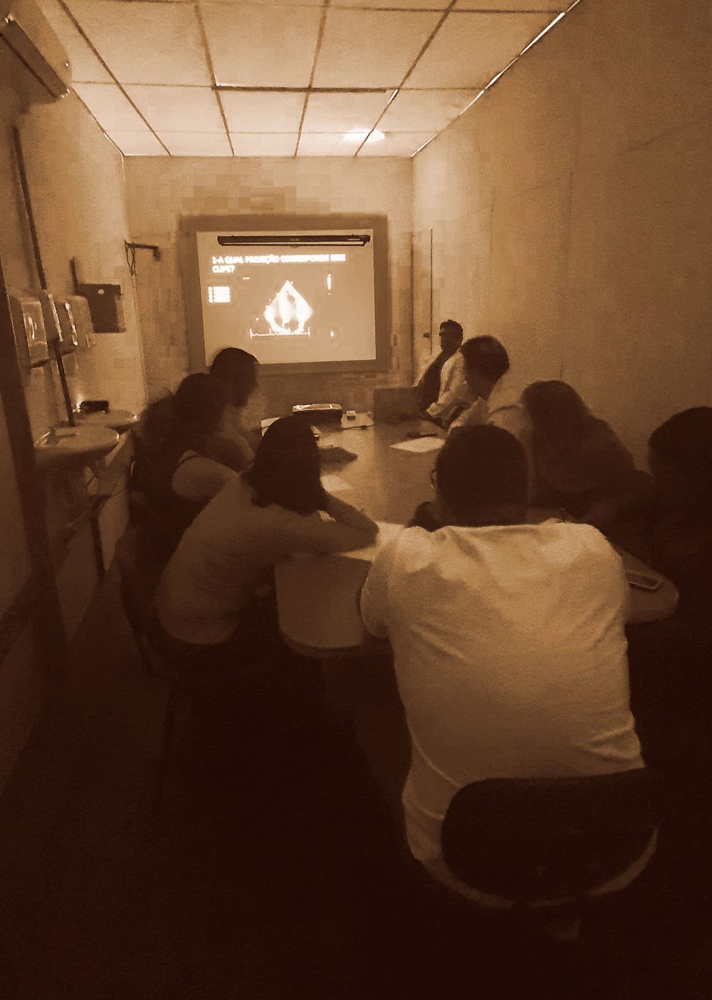 Pessoas em uma sala assistindo a uma apresentação em uma tela.