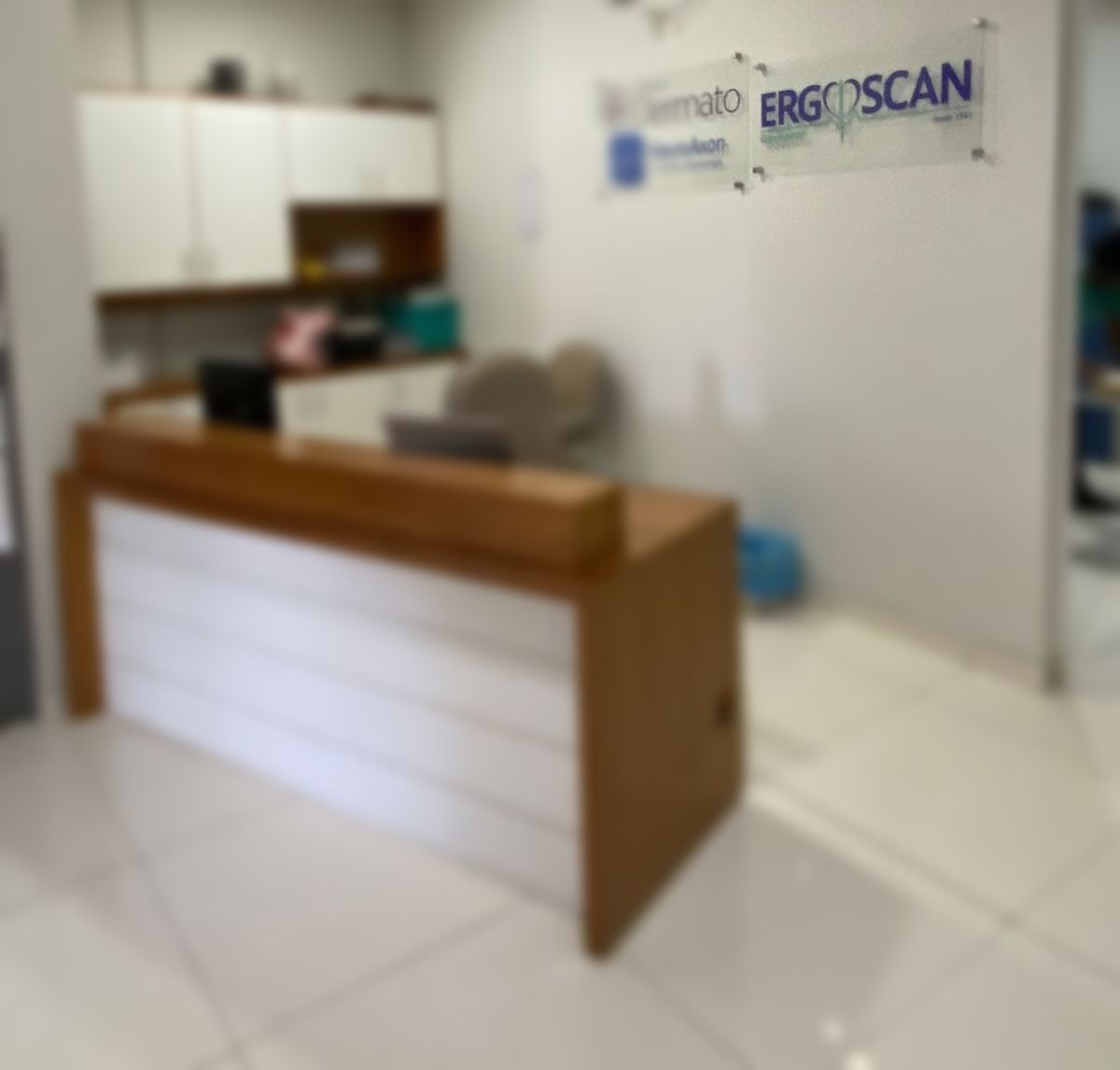 Balcão de recepção com frente branca e acabamento em madeira; placa ErgoScan ao fundo.