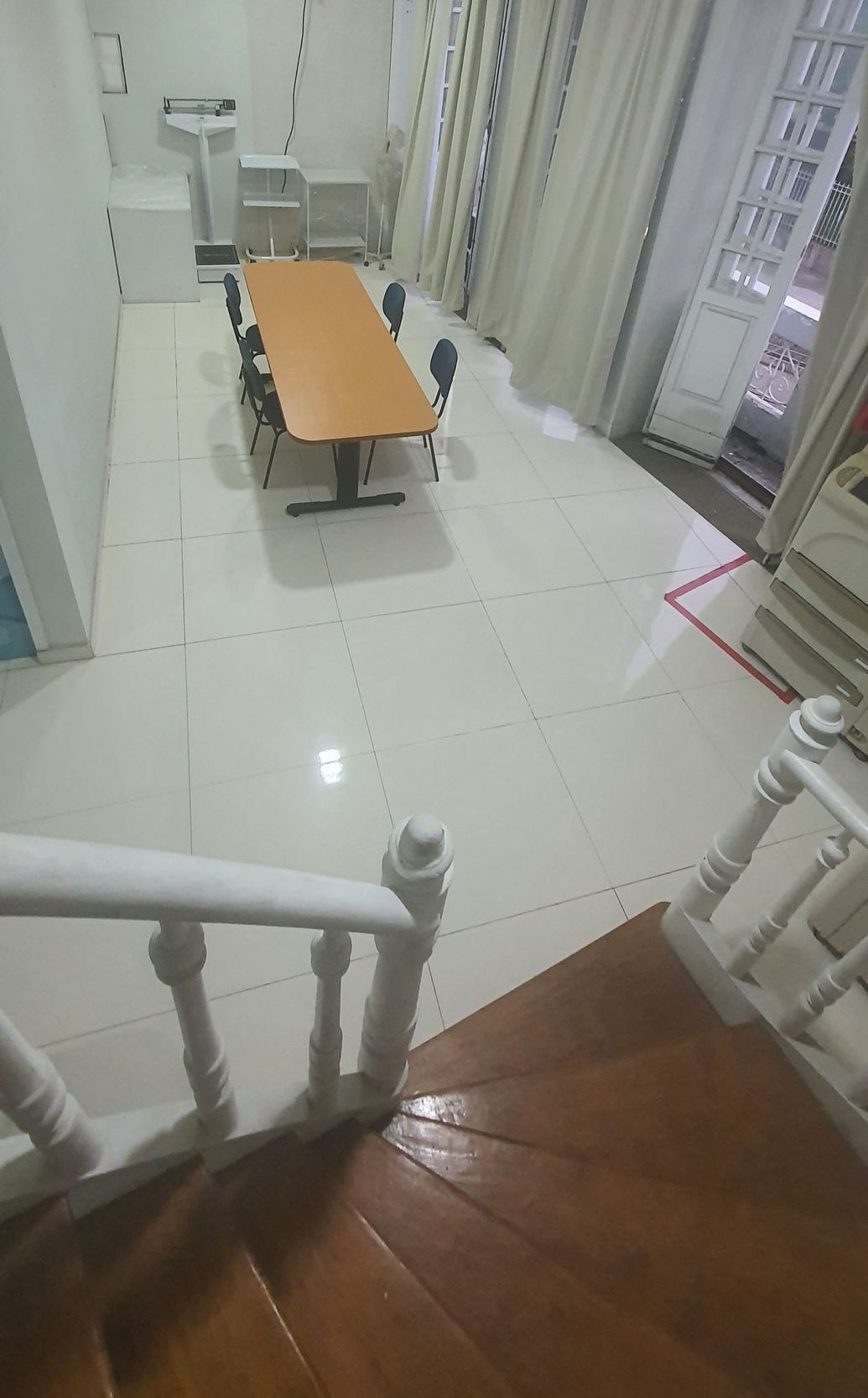 Uma escada leva a uma sala com uma mesa comprida, cadeiras e uma janela com cortinas brancas.