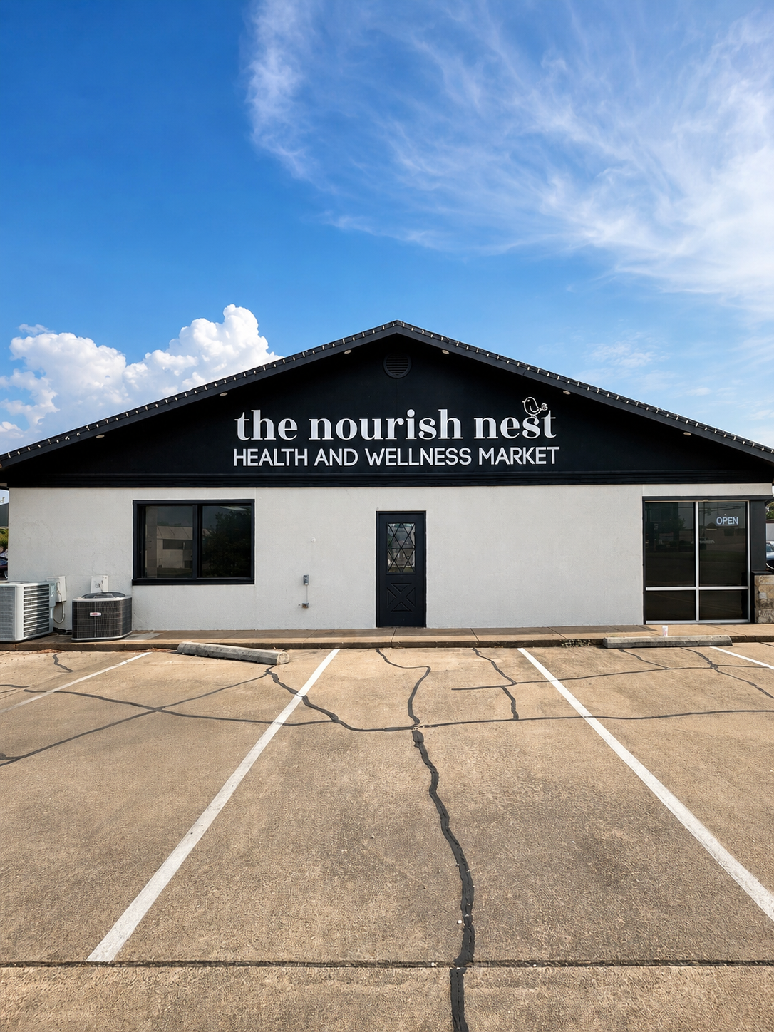 Storefront of The Nourish Nest Health and Wellness Market with a black sign and parking lot in front