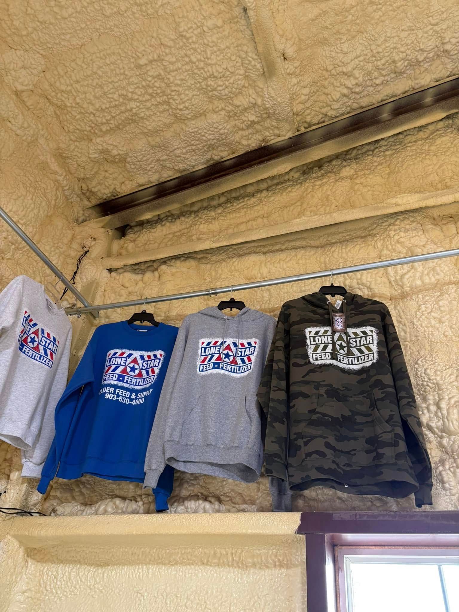 Four graphic T-shirts hanging on a line under a rough ceiling, in blue, gray, and dark camouflage.