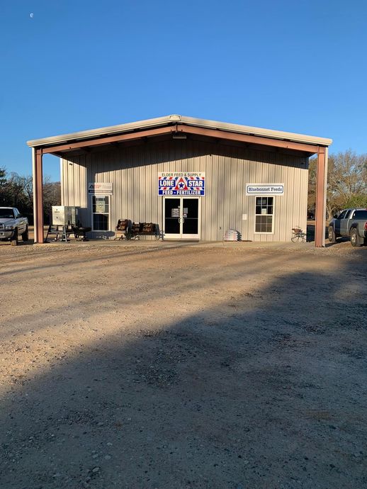 Small rustic storefront with a tan exterior, large garage-style door, and gravel lot under a clear blue sky