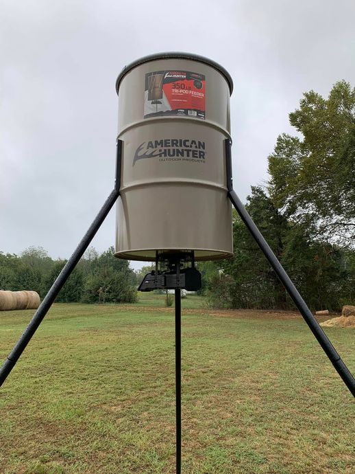 Outdoor silver grain silo on black legs in a grassy field under cloudy sky
