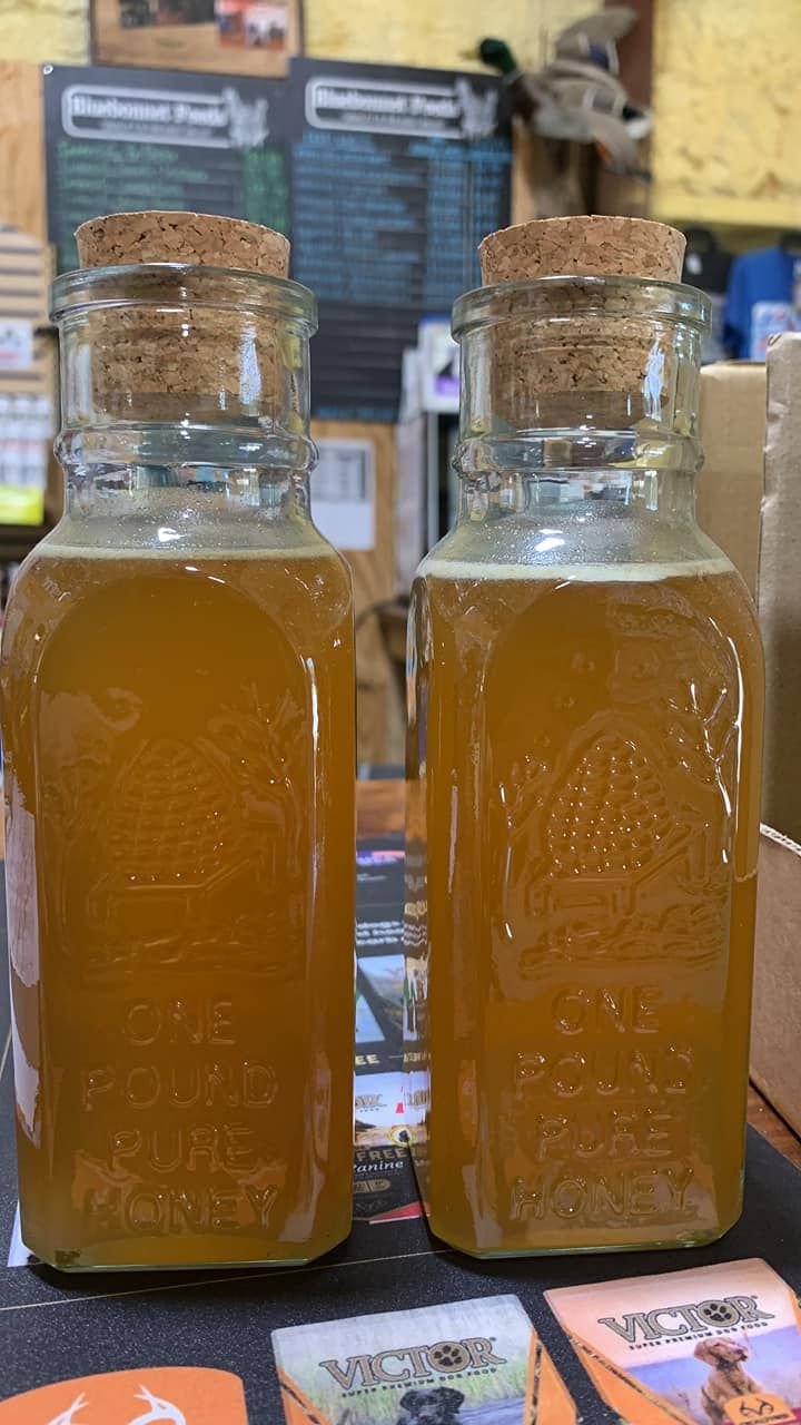 Two corked glass bottles filled with amber liquid on a market counter, with a blurry menu board behind.