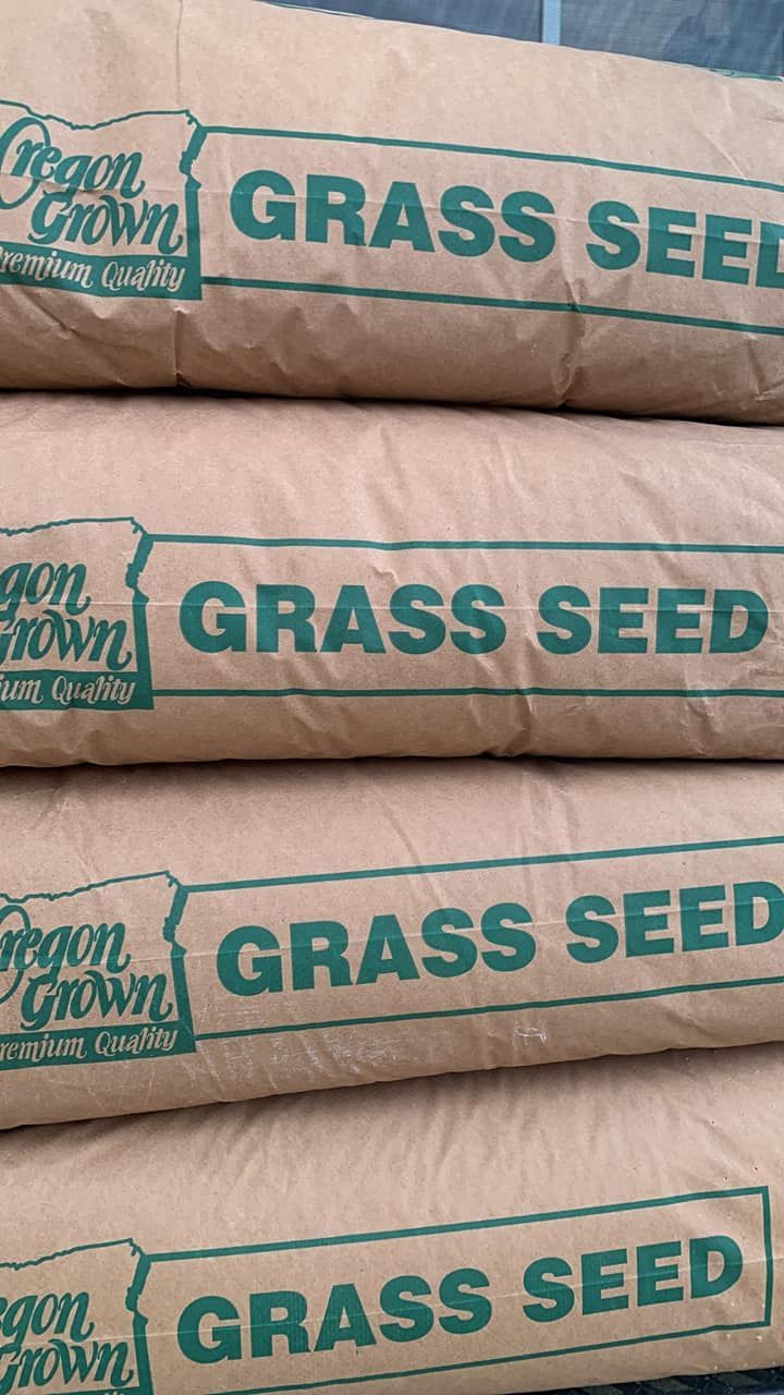Stacked beige bags labeled “GRASS SEED” on a wooden surface.