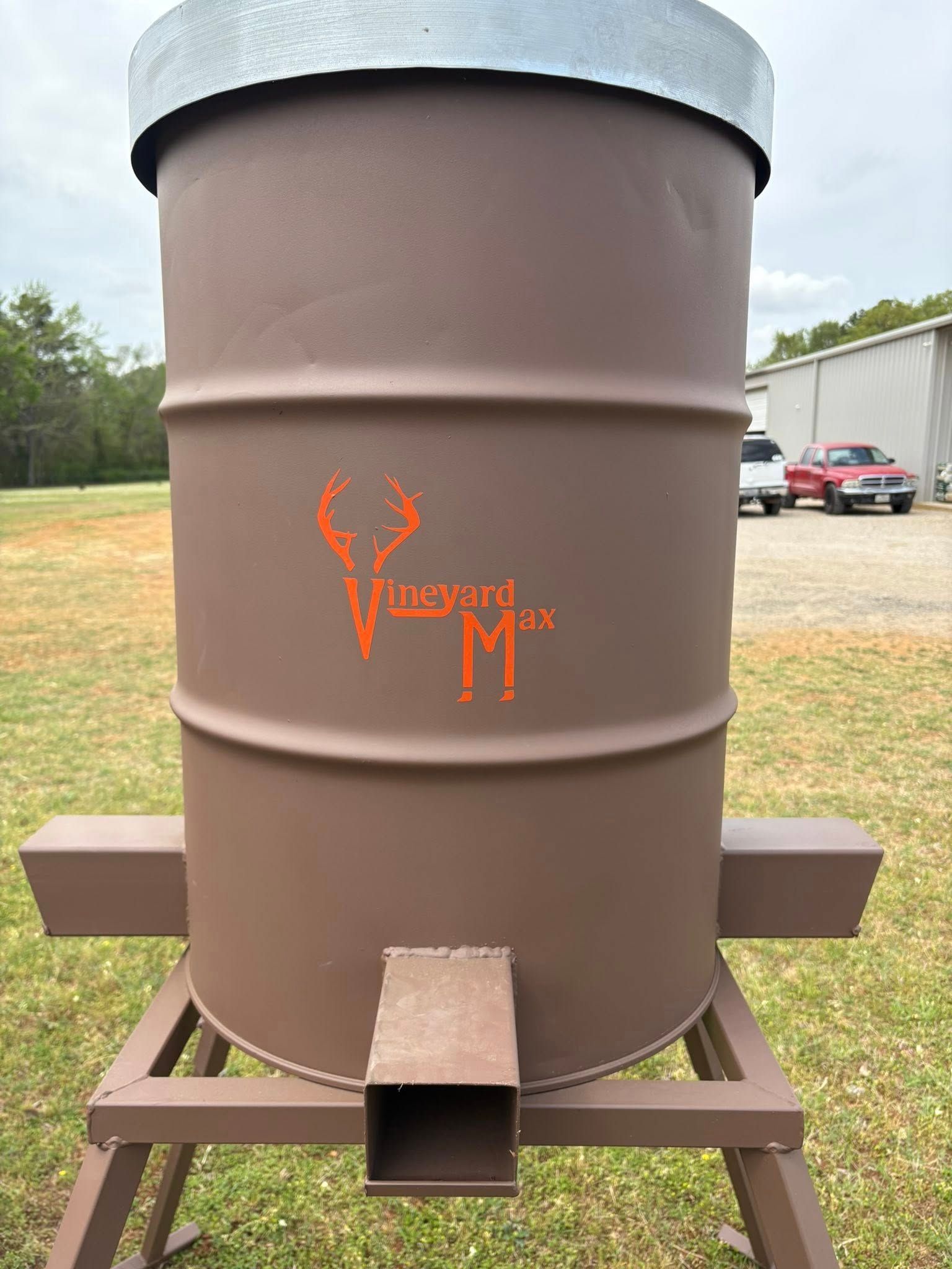 Brown outdoor smoker/grill with a black lid and orange logo on a metal stand in a yard
