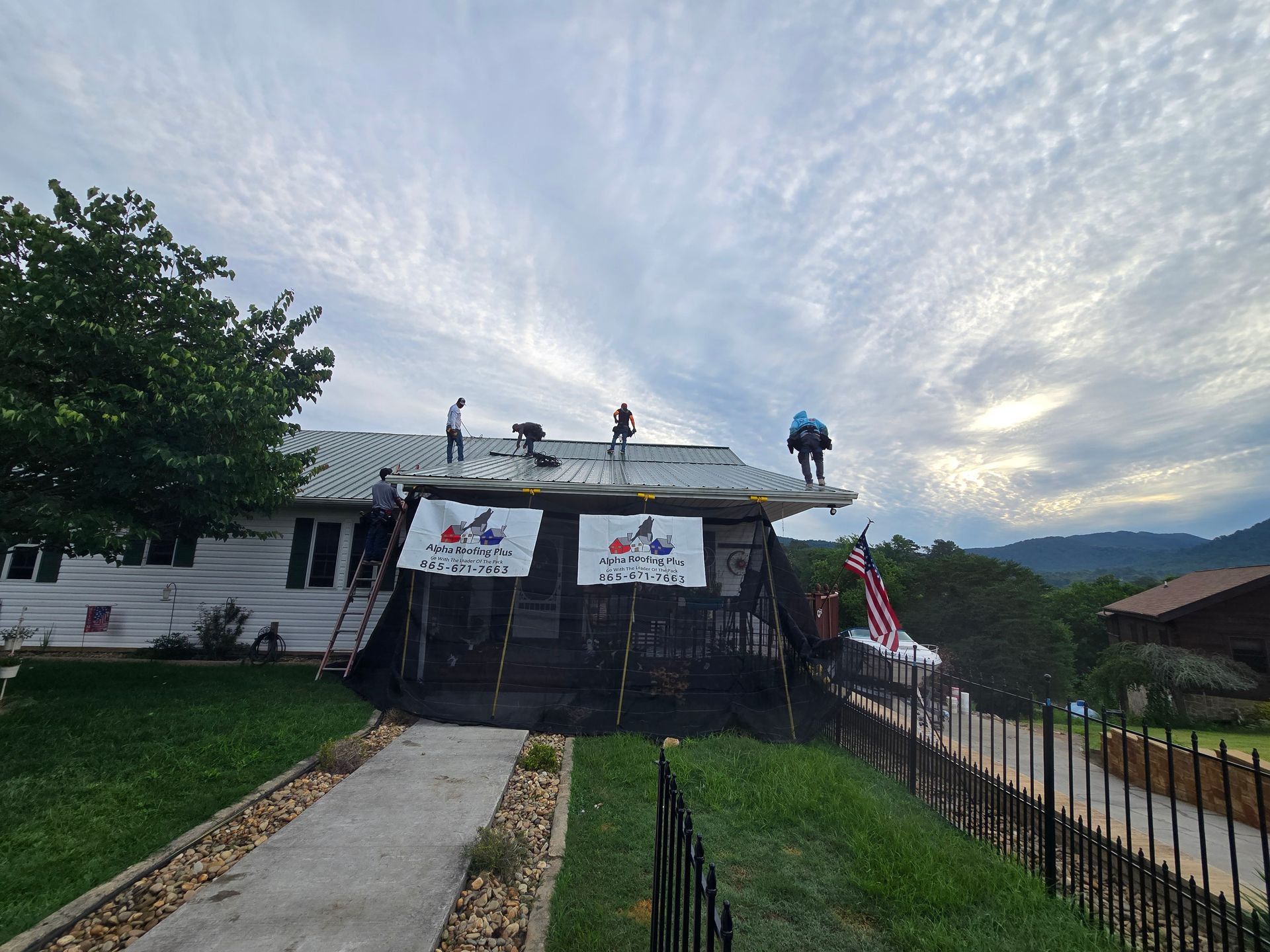 Two workers in safety vests and helmets installing metal roofing on a sloped roof
