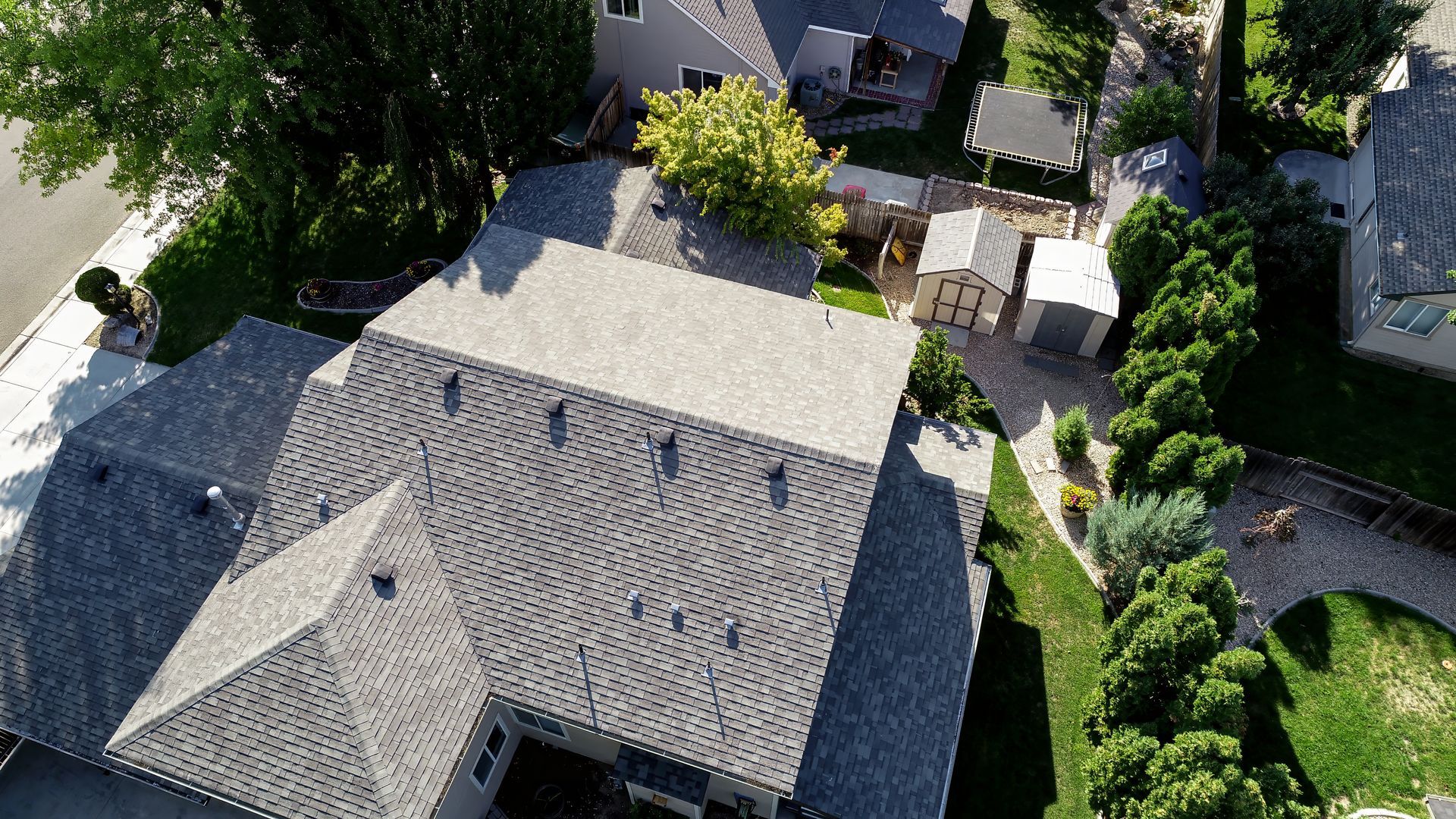 Aerial view of a house with a gray roof, surrounded by trees, a driveway, and a backyard patio.