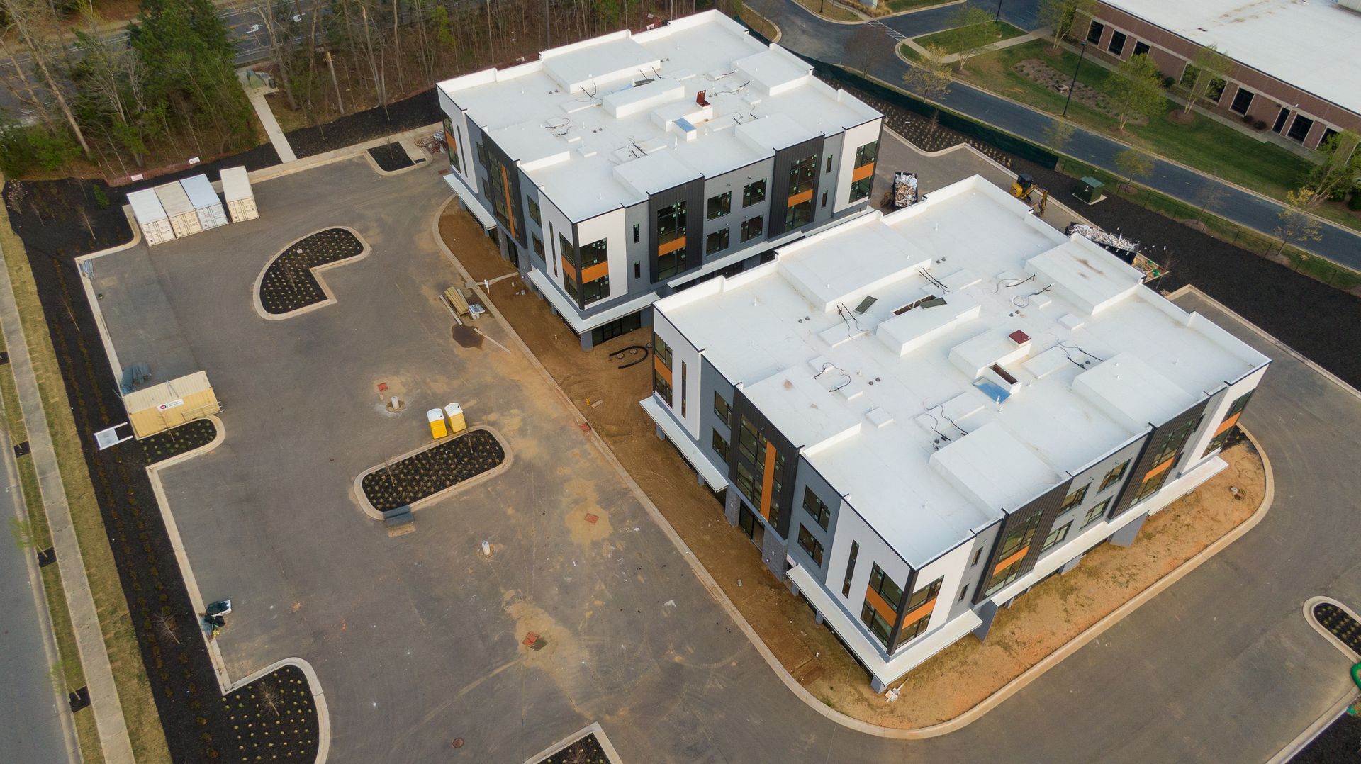 Aerial view of two modern white buildings beside a mostly empty parking lot and road.