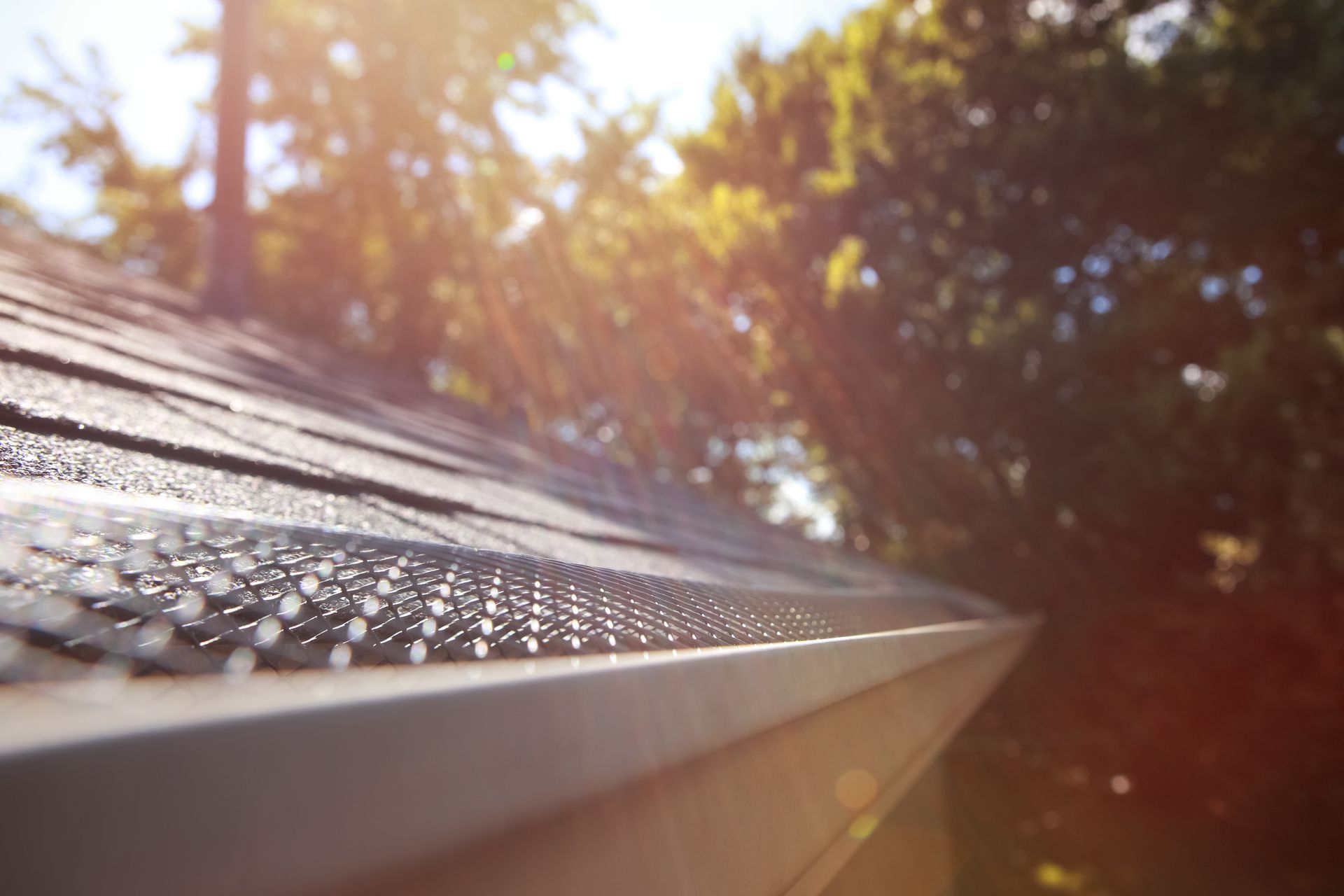 Roofer installing dark gray shingles on a sloped roof beside a brick chimney, with tools nearby