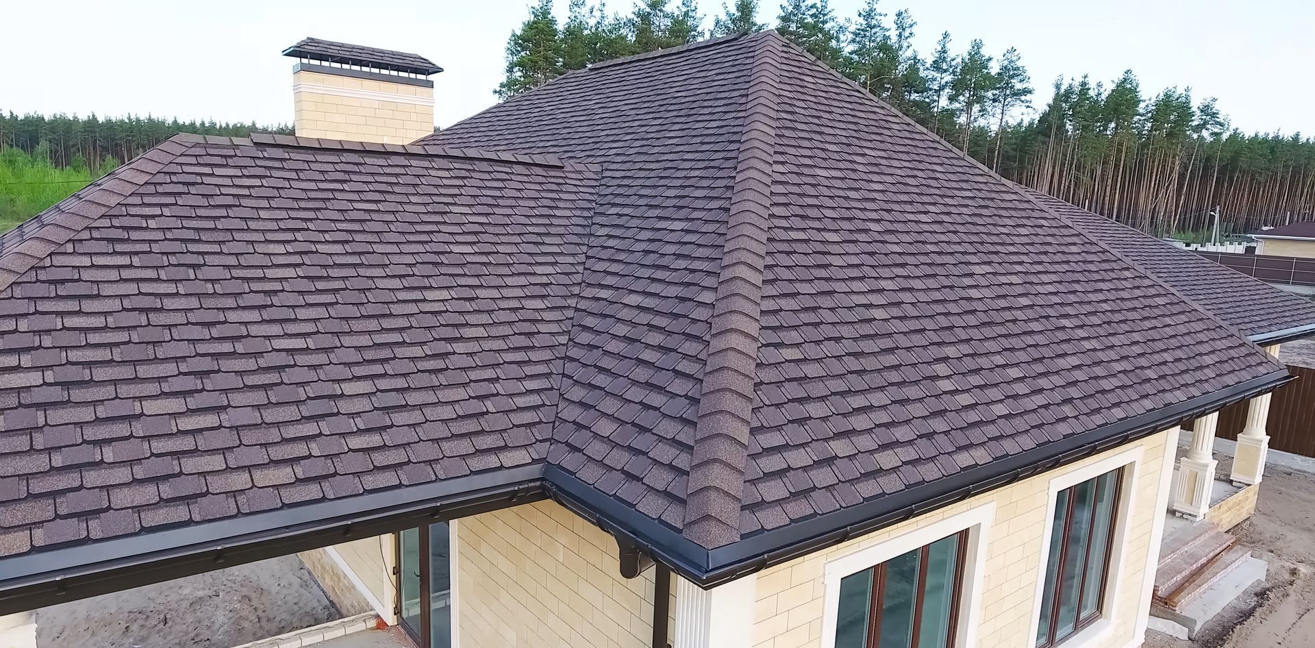 Aerial view of a house with a dark shingled hip roof and chimney