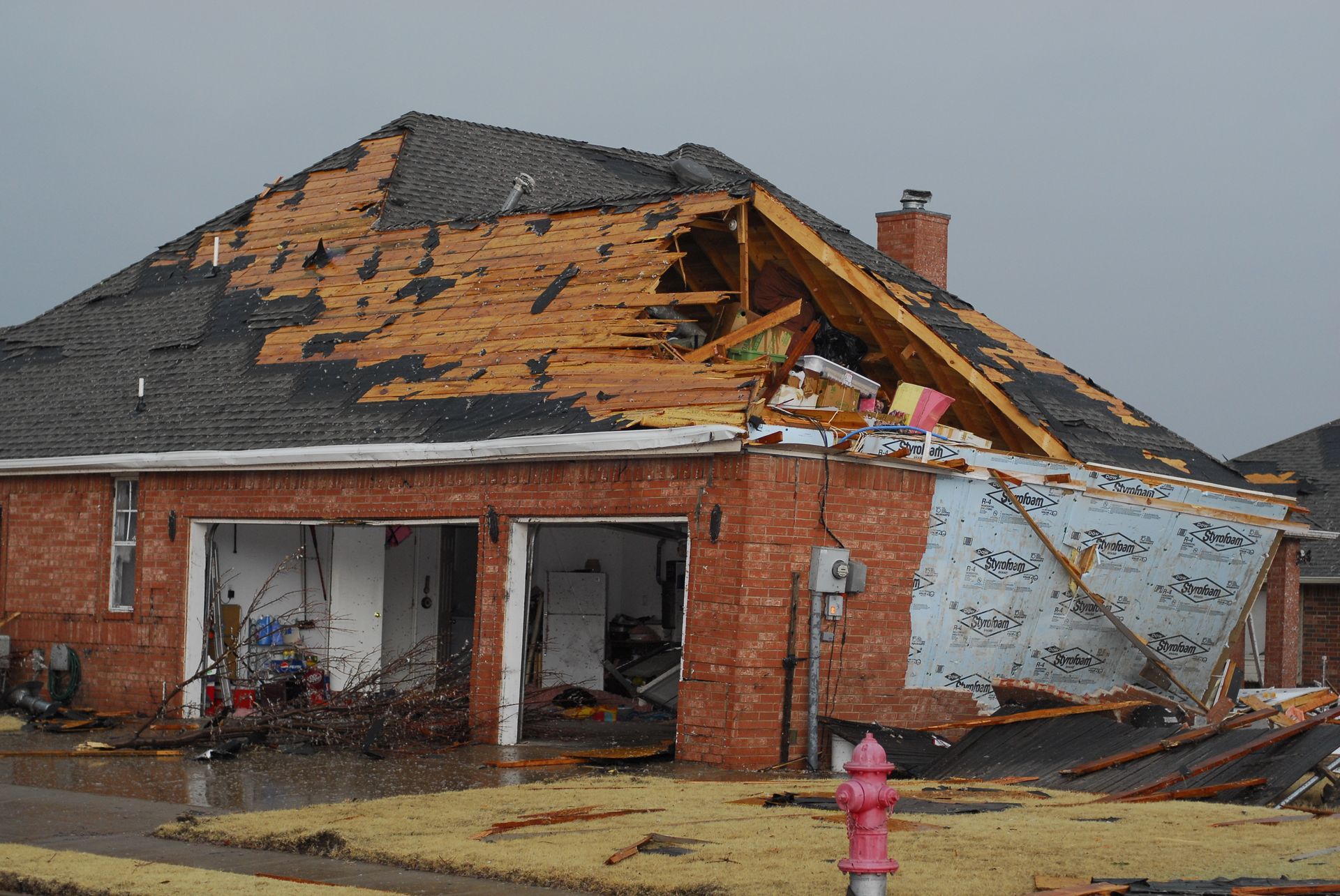 Damaged brick house with torn roof and debris after storm, fire hydrant in front