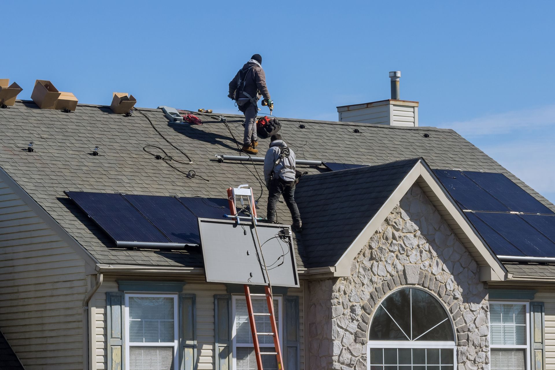 Roofers repairing a house roof with solar panels and a ladder in place