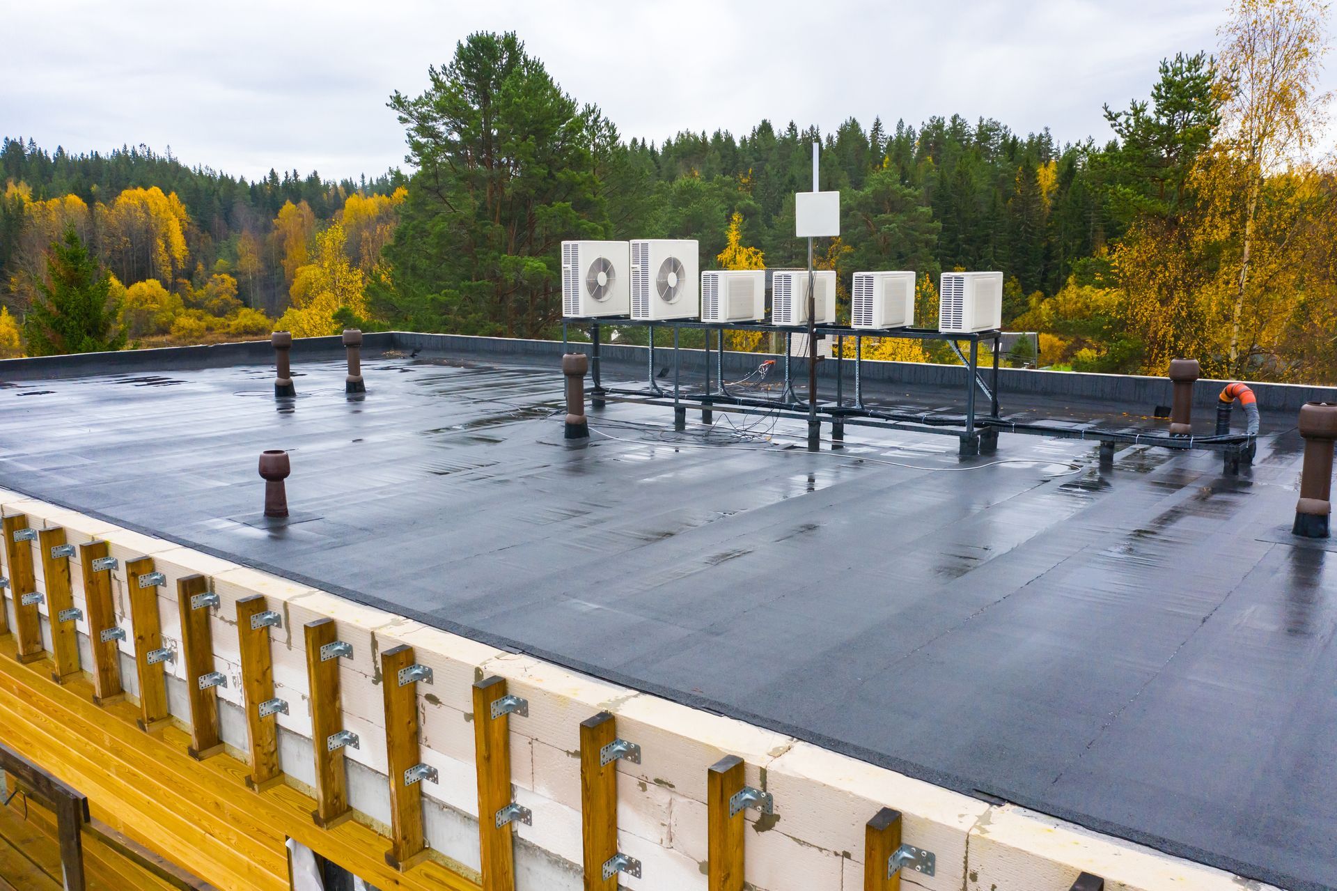 Industrial rooftop with black waterproof membrane and equipment, surrounded by autumn trees