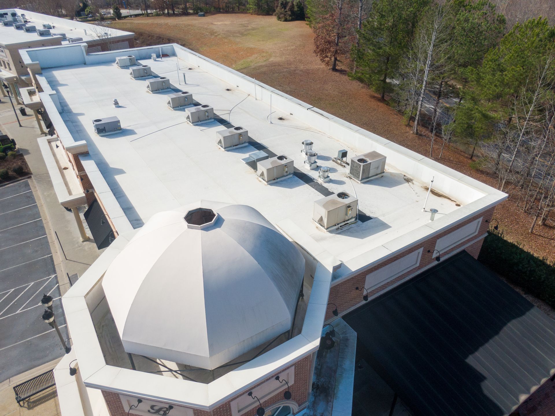 Aerial view of a white-roofed building with rooftop HVAC units and a dome entrance.