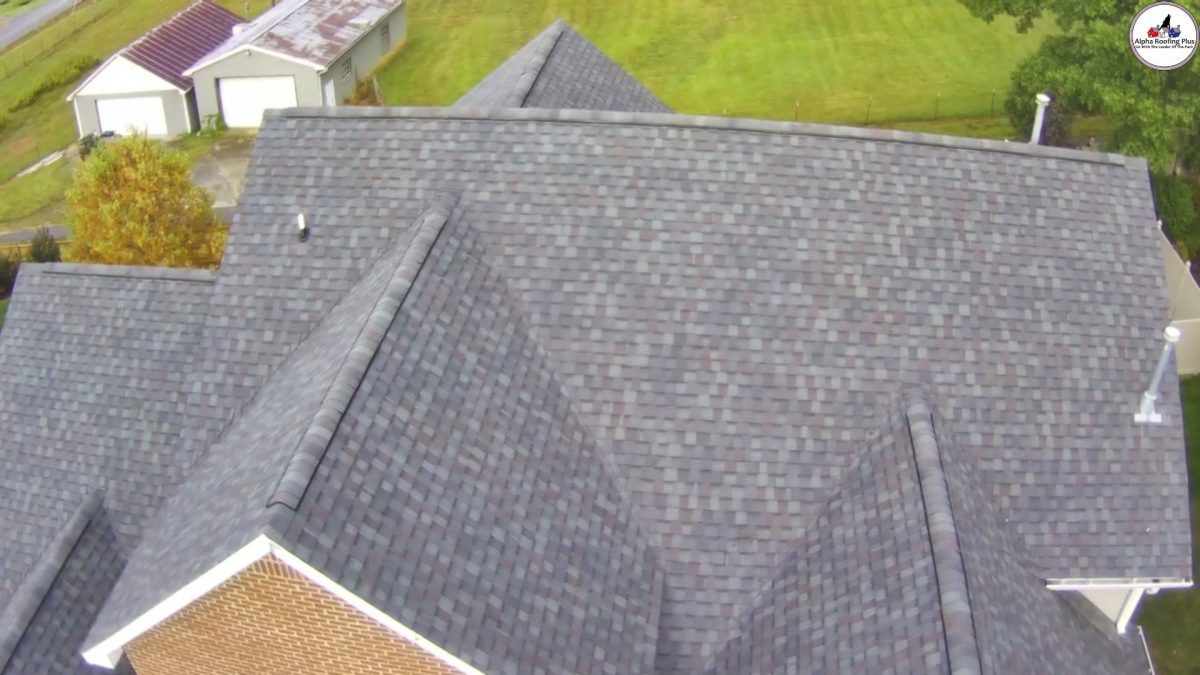 Aerial view of a gray shingled house roof with surrounding lawn and nearby buildings.