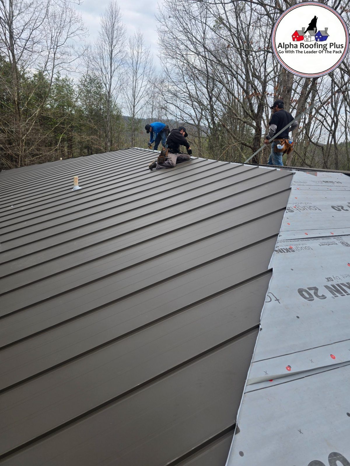Workers installing gray metal roofing on a house roof under construction