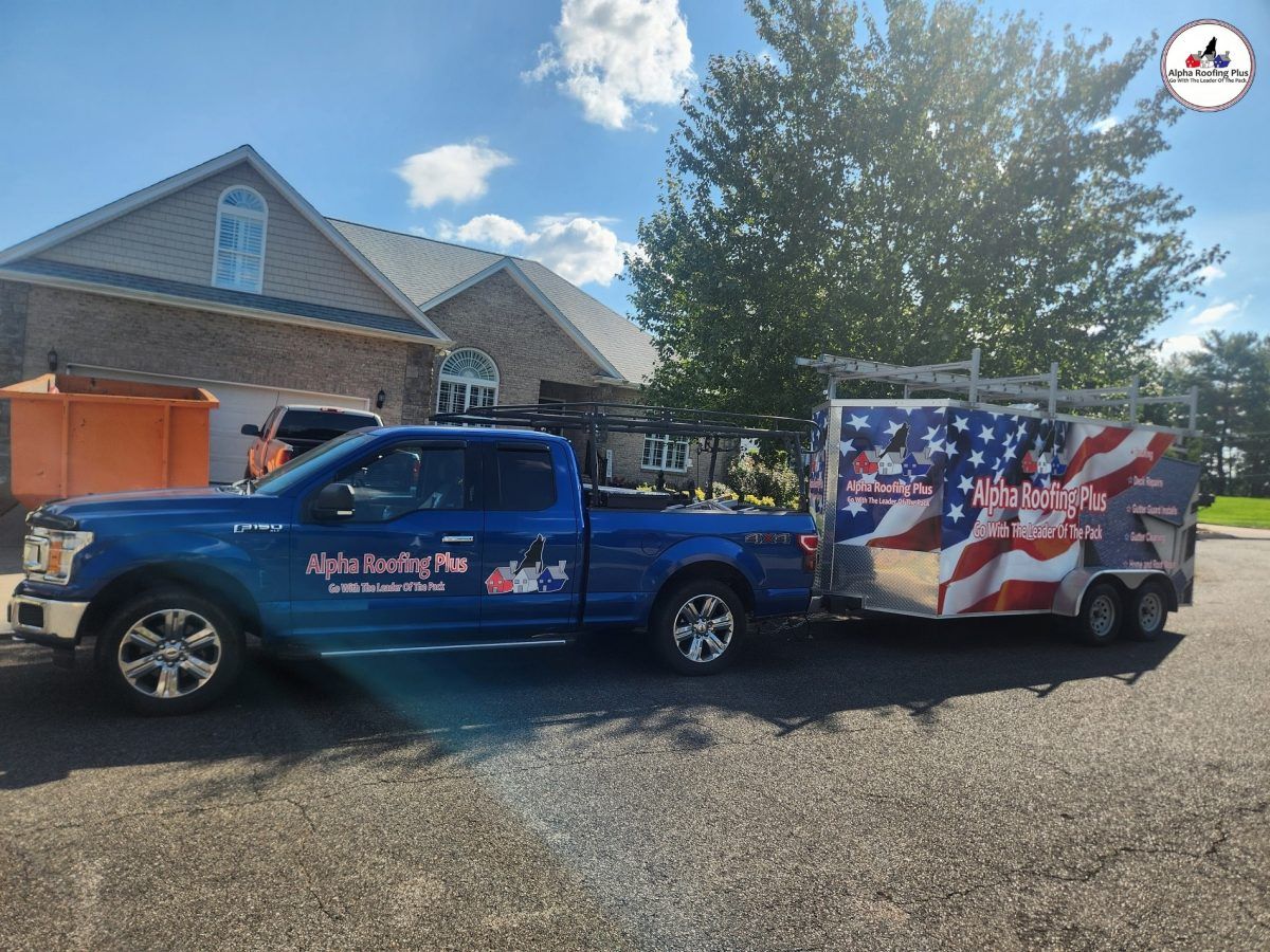 Blue pickup truck towing a patriotic flag-covered trailer in a driveway beside a brick house