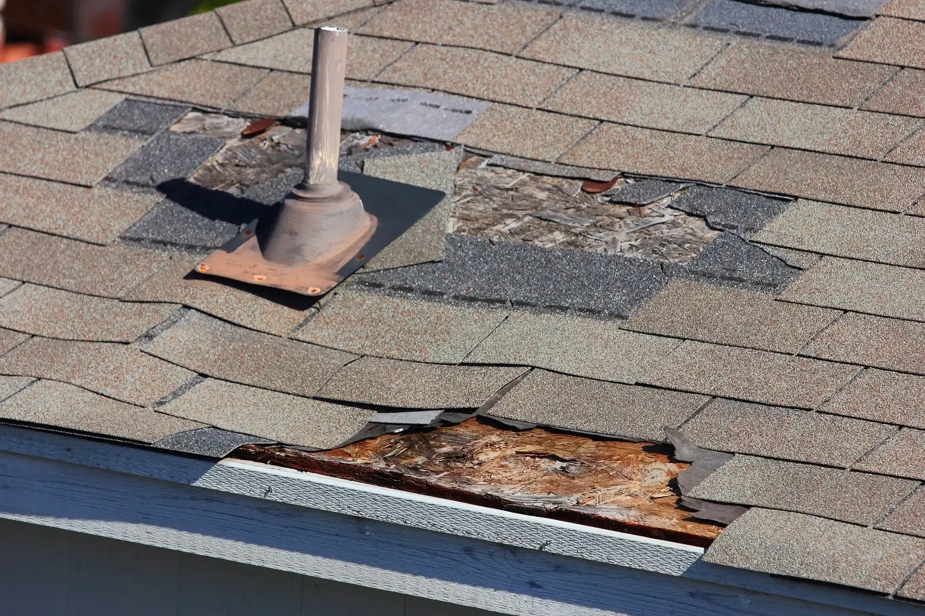 Damaged shingle roof with a vent pipe and a rusted, exposed hole near the eave