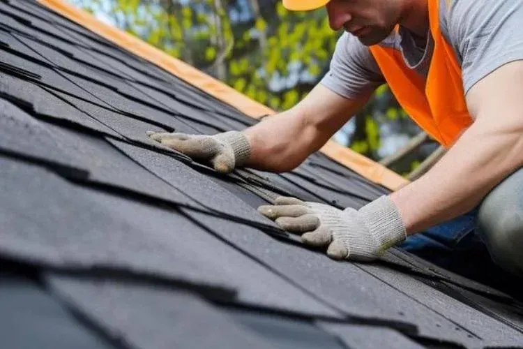 Worker in orange vest installing dark shingles on a roof
