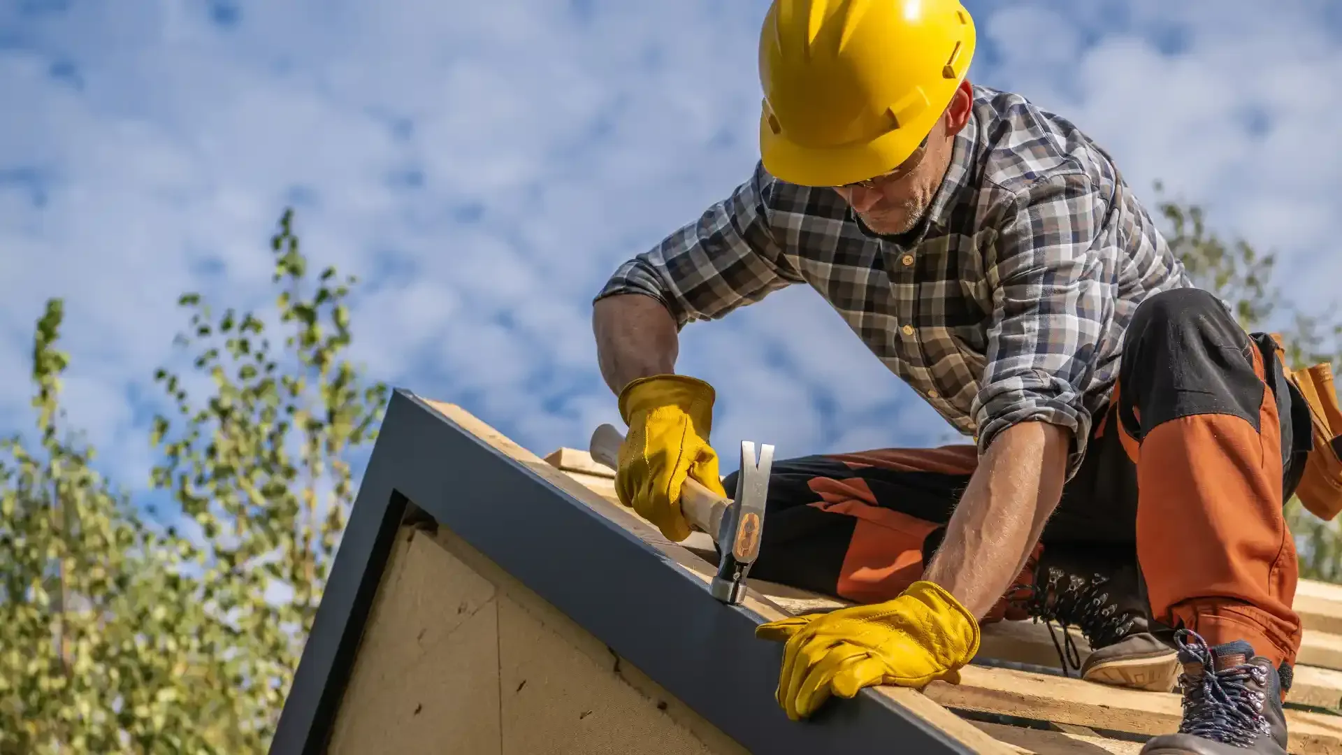 Construction worker in yellow hard hat measuring roof shingles on a house