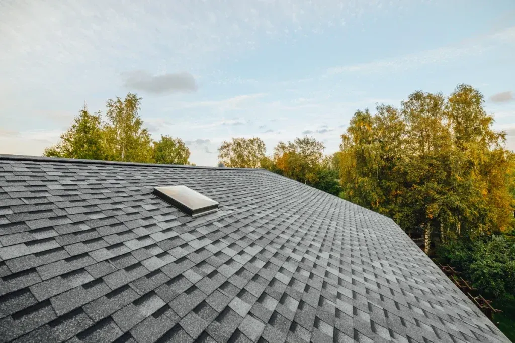 Red tiled house roof with skylight beneath a bright blue sky and white clouds