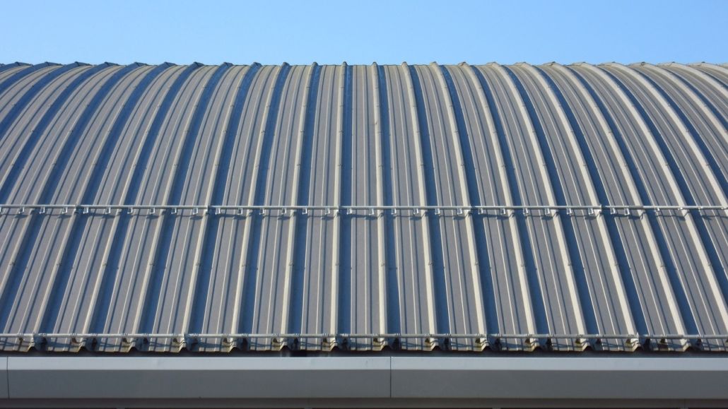 Curved corrugated metal roof with alternating blue and white stripes against a pale sky