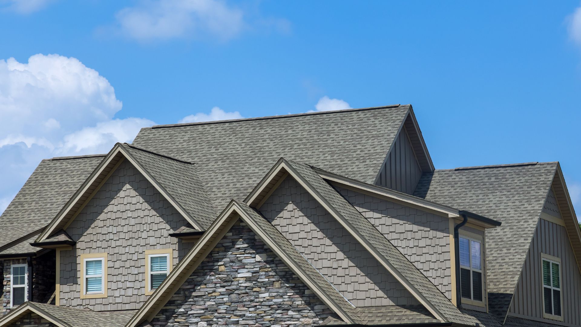 Gray shingled house roofs with dormers against a blue sky and clouds