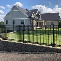 Gray house with black metal fence and green lawn.
