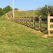 Wooden fence on grassy hill against a blue sky, leading to a distant structure.