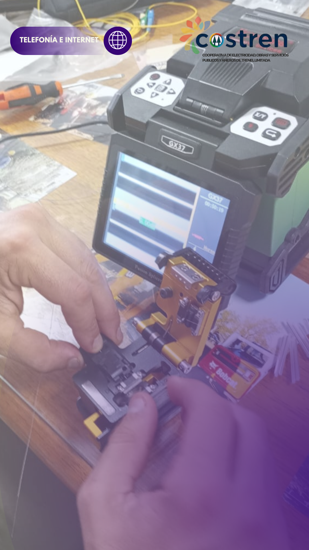 Manos trabajando con equipos de fibra óptica, realizando un empalme de fusión en un entorno bien iluminado.
