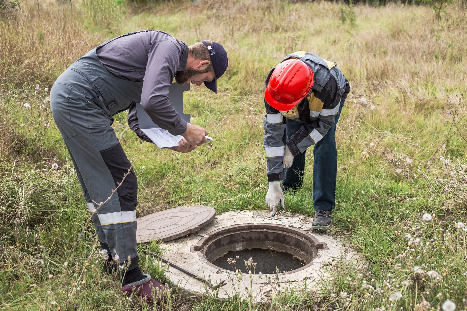 Inspectors examining an open septic system access point in a field. Inspectors examining an open septic system access point in a field.