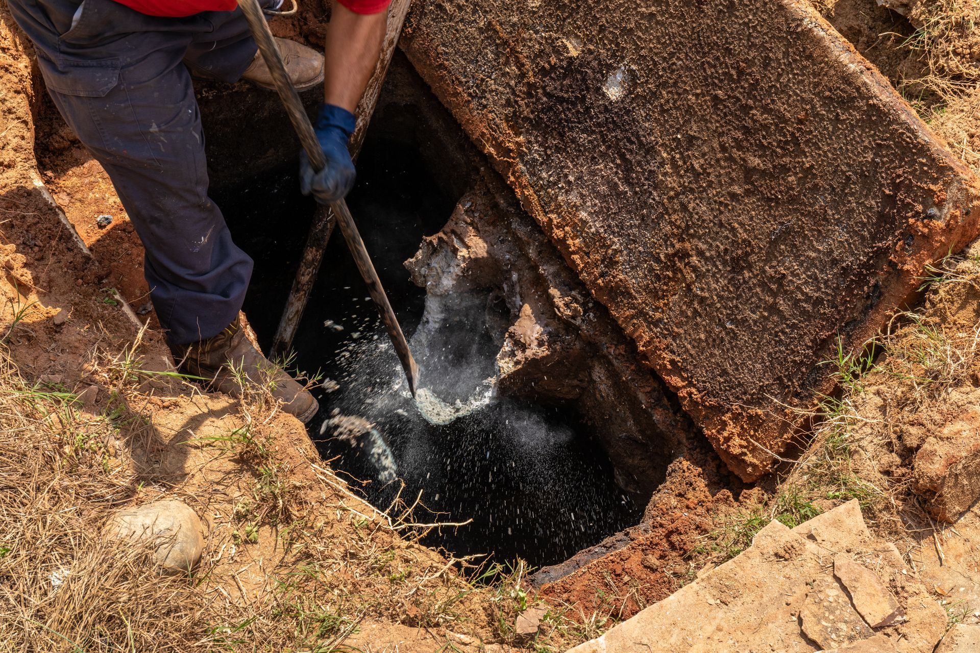 Worker inspecting and clearing a septic tank opening during maintenance. Worker inspecting and clearing a septic tank opening during maintenance.