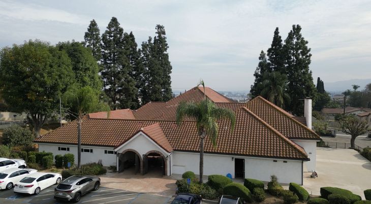 The ACCN La Puente Church Building. White stucco building with a red tile roof, arched entrance, and parked cars among trees