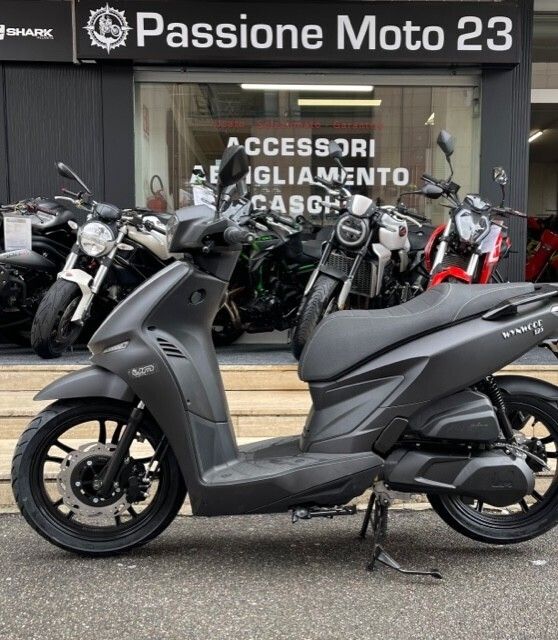 Uno scooter nero parcheggiato davanti a un negozio di motociclette, con altre motociclette visibili.